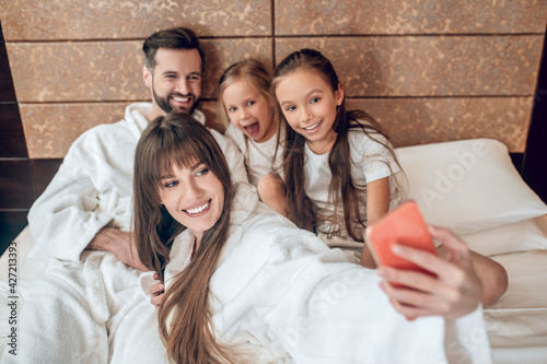 Family in white robes lying in bed and making selfie