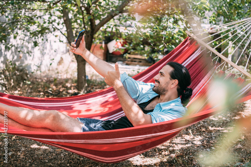A young man is resting and talking on the phone in a hammock in the garden
