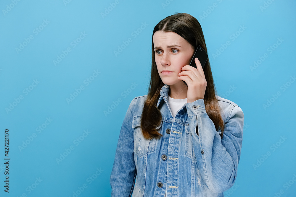 Concerned young woman talking on smartphone solving problems, worried girl discussing business issue speaking by cell mobile making call having difficult conversation, isolated on blue studio wall Concerned young woman talking on smartphone solving problems, worried girl discussing business issue speaking by cell mobile making call having difficult conversation, isolated on blue studio wall