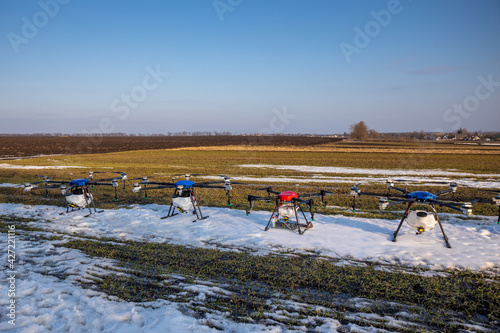 Many agrodrones are on the green field. The snow has not melted yet. Agrodrons are ready to spray fertilizer.