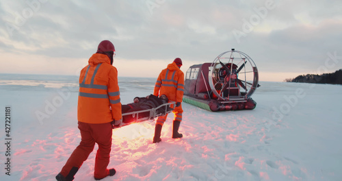 Rescue service team loading victim on stretcher in air-boat patrolling coast in winter