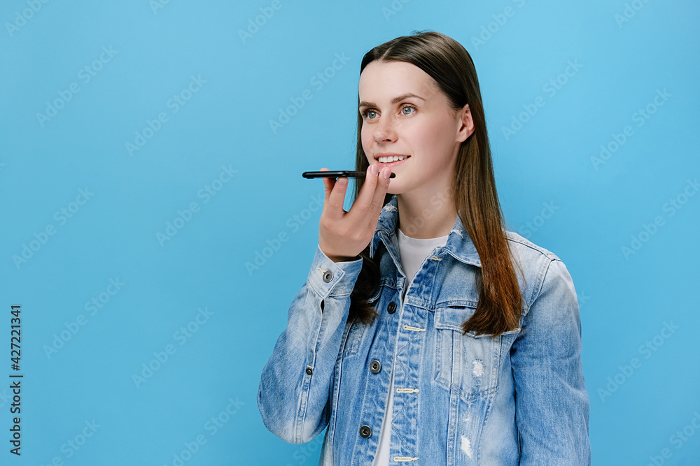 Millennial female holding phone speak activate virtual digital voice assistant on smartphone, girl recording voice message, chatting with friends online or speakerphone, isolated on blue background Millennial female holding phone speak activate virtual digital voice assistant on smartphone, girl recording voice message, chatting with friends online or speakerphone, isolated on blue background