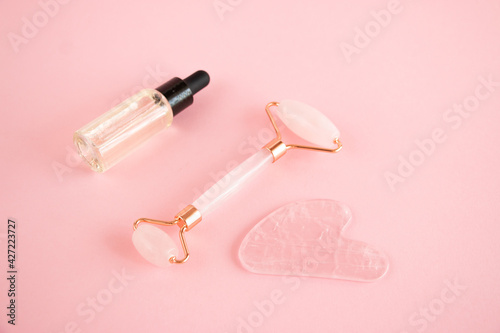 Pink quartz roller for facial massage and a jar of cosmetic serum on a pink background. Beauty and home skin care concept. Anti-aging therapy and lifting.