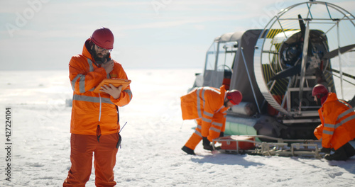 Coast guard team standing on frozen lake with hovercraft on background