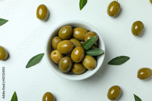 Bowl of green olives and leaves on white background, top view