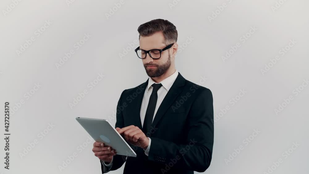 Confident young man in formalwear working on digital tablet while standing against grey background