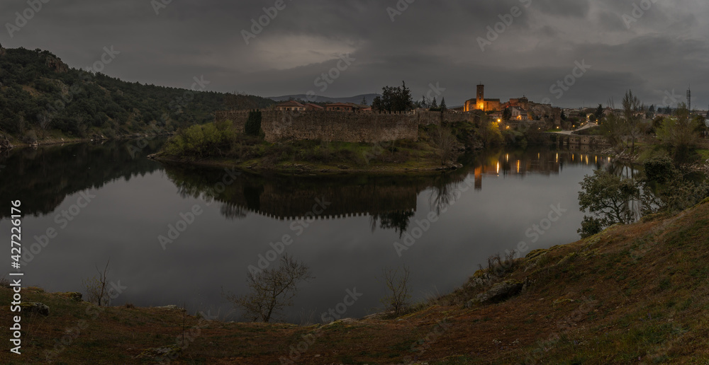 Sunrise of a village with lights, a Romanesque wall with a church tower at night in panoramic picture