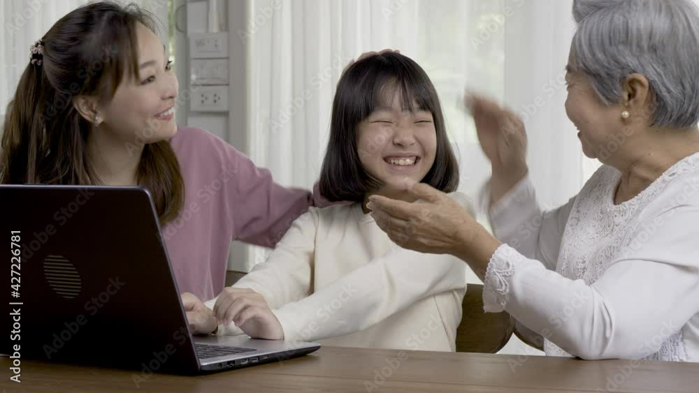 A girl looking to computer with smiling. She was happy that she passed the exam. Mother and grandmother congratulate with her. Online study concept.