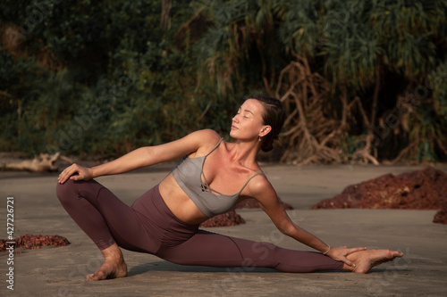 A girl practicing yoga on the beach green and brown background with jungles and rocks behind 