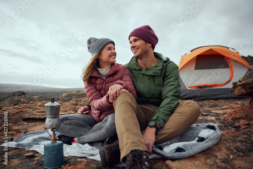 Smiling young man and woman looking at each other with love and preparing morning drink at campsite during winter