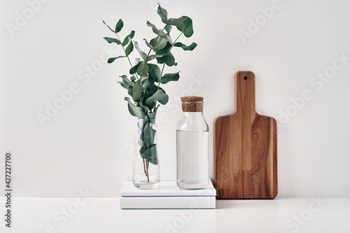 A transparent bottle with a cork stopper, a vase with eucalyptus branches and a wooden board. Natural and eco-friendly materials in interior decor. Copy space, mock up.
