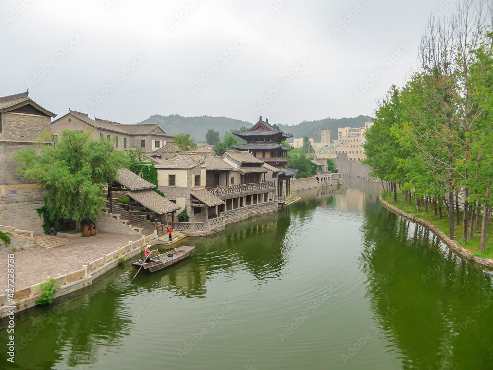 A view on the river in a small village in northern China. The river is overgrown with green plankton. Houses on both sides of the river. Serenity and calmness. Overcast due to the air pollution