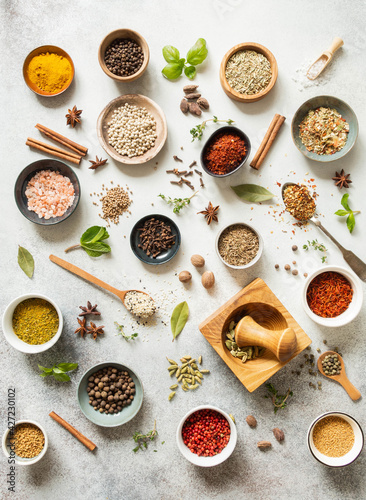 Various dry spices in small bowls and raw herbs flat lay on grey background.