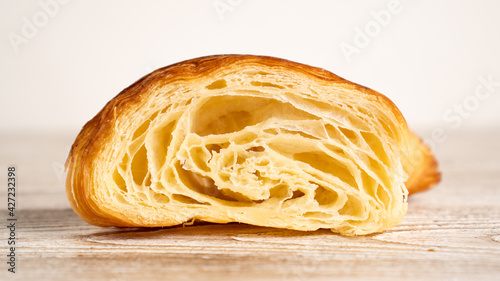 Freshly baked croissant cut in half on light wooden table. Croissant in the center of image
