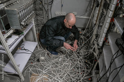 A technician sits on wires in a ransacked server room. The man reconnects at the abandoned datacenter. An engineer repairs equipment of an old TV station