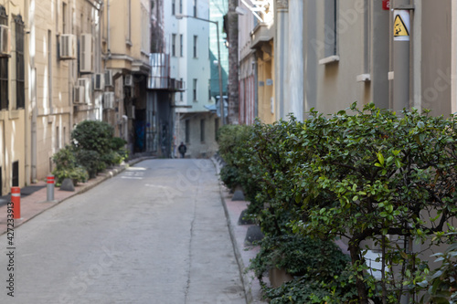 A long shady street in the European part of Istanbul, along which there is a shrub growing. The houses are gray and yellow. Air conditioners hang on the walls. © Vadim