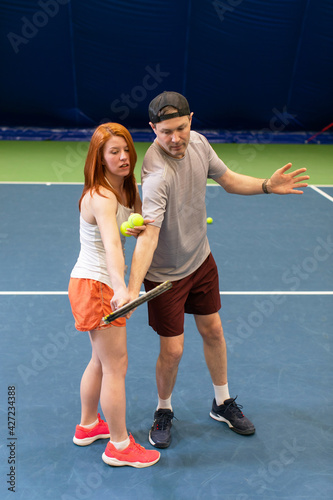 Tennis player getting instruction from coach how to play game on a court indoor. Female instructor observes her student's playing and pitch technique