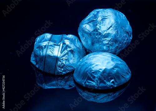 Praline candies in a white wrapper on a dark blue mirror background. Candy with a mirror image on the background. Isolated.
