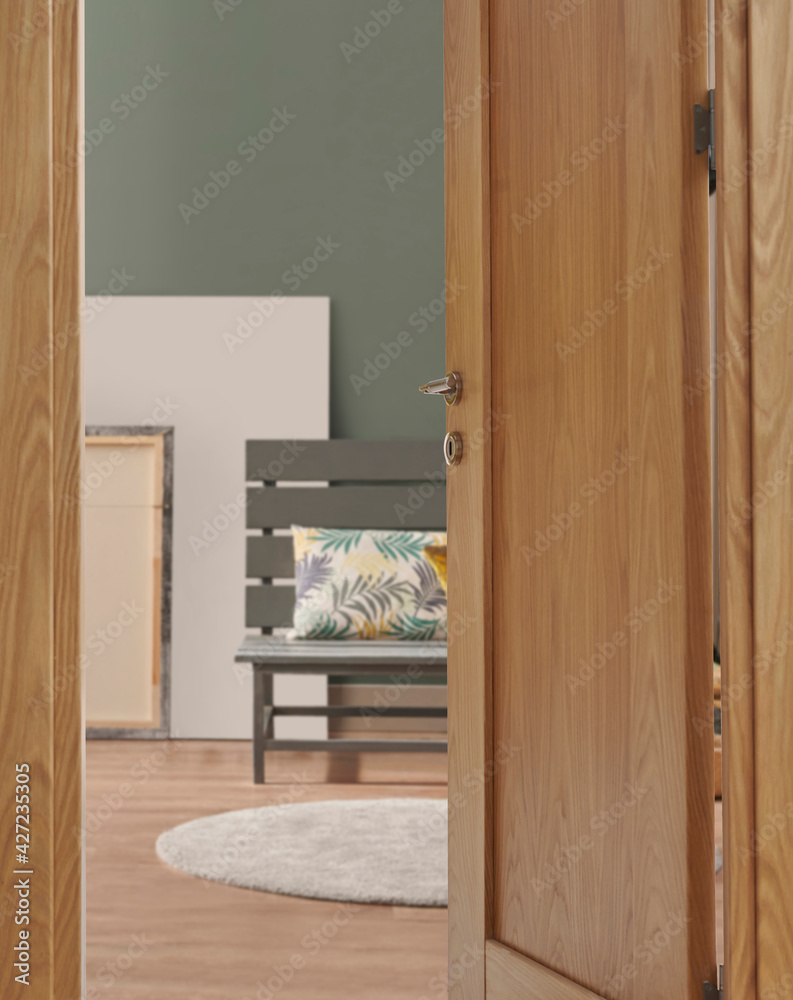 Close up wooden door, green interior room wall background and decorative luxury wood concept, bike, grey chair pillow and carpet design, black lamp with poster and frame.