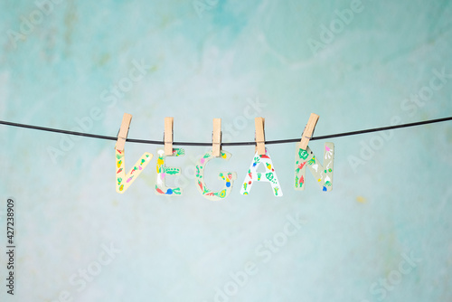 Word VEGAN in wooden letters painted with vegetables and hung with clothespins on a rope on a Green background. Health Concept