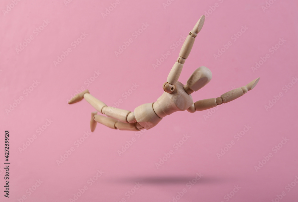 Falling down wooden puppet on pink background