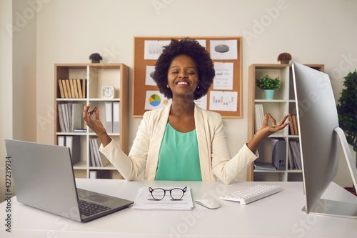 Happy employee getting ready to start productive work day. Young business woman sitting at office desk and meditating eyes closed thinking of good things and focusing on positive feelings and emotions
