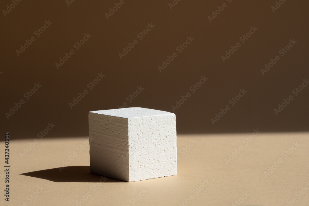 3d podium, for presentations of packaging and cosmetics. White foam cube with a hard shadow from natural light, on a brown background. The concept of the beauty industry 3d podium, for presentations of packaging and cosmetics. White foam cube with a hard shadow from natural light, on a brown background. The concept of the beauty industry