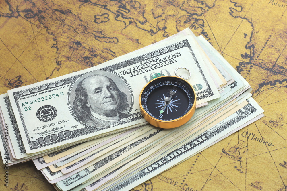Classic navigation compass on background of old world map and american dollars as symbol of tourism with compass, travel with compass and outdoor activities with compass