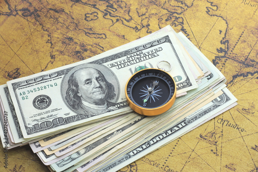 Classic navigation compass on background of old world map and american dollars as symbol of tourism with compass, travel with compass and outdoor activities with compass Classic navigation compass on background of old world map and american dollars as symbol of tourism with compass, travel with compass and outdoor activities with compass