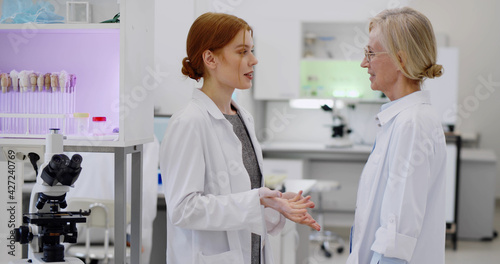 Young female scientist discussing result of virus research with supervisor in laboratory