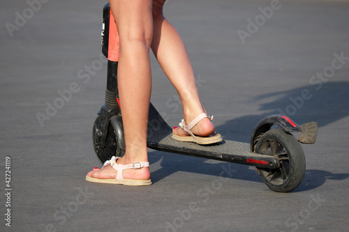 Girl rides electric scooter on a city street, female legs on asphalt. Riding e-scooter in spring or summer season
