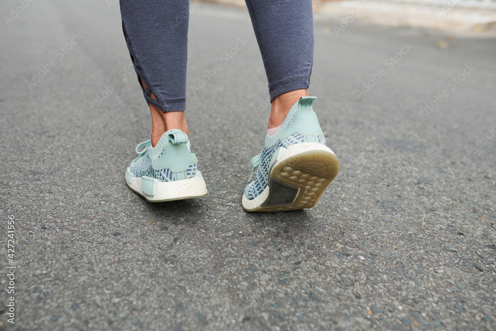 Feet of female runner jooging on asphalt road outdoors in the morning when training for marathon
