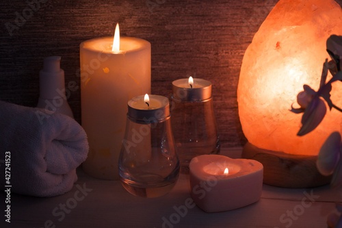 Himalayan salt lamp with orchid flower, oil, towel, candles in dark room. Spa, relax concept.