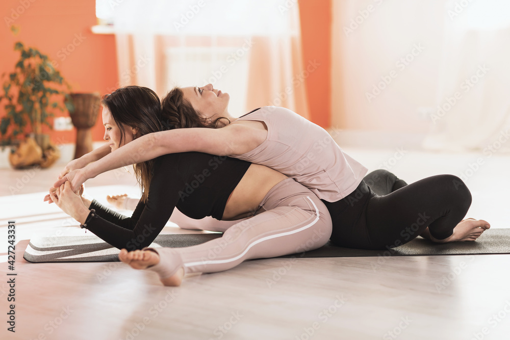 Two women doing Upavishta Konasana and Baddha Konasana bends sitting on a mat in a yoga studio, personal training