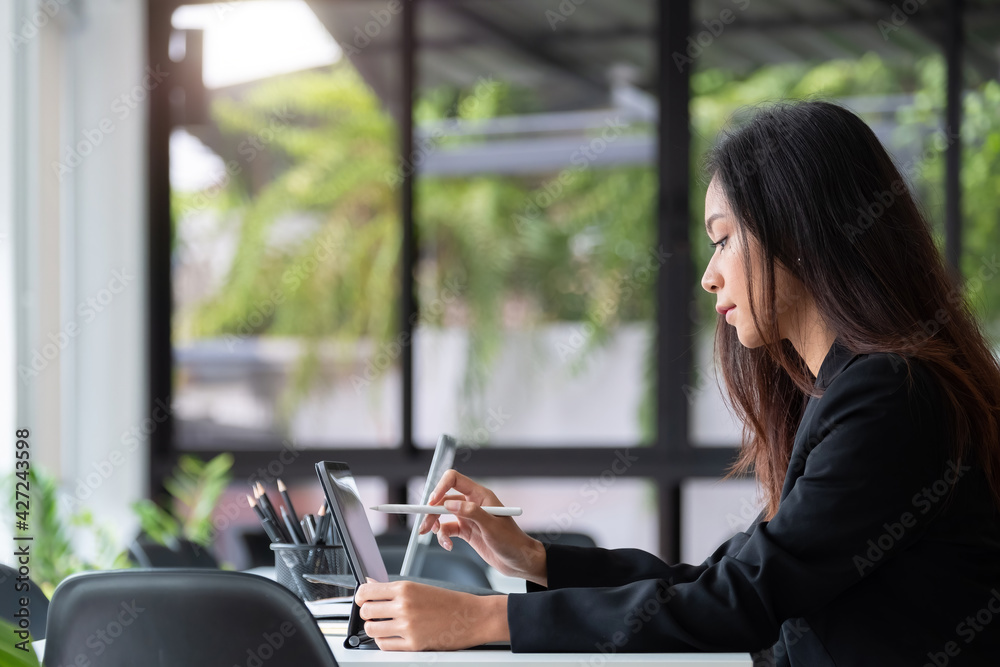 Young asian woman using digital tablet with pen stylus while sitting at her office desk in modern office Young asian woman using digital tablet with pen stylus while sitting at her office desk in modern office