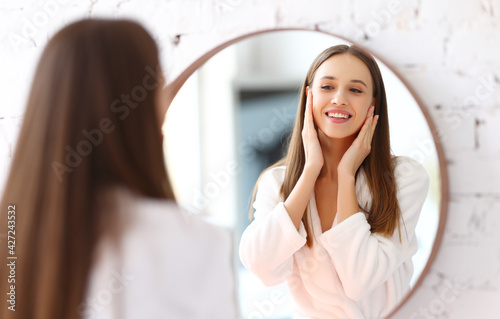 Smiling woman applying facial cream near mirror