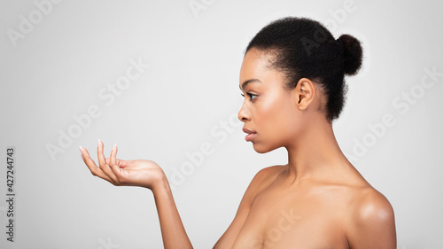 Serious African Lady Looking At Invisible Product In Hand, Studio