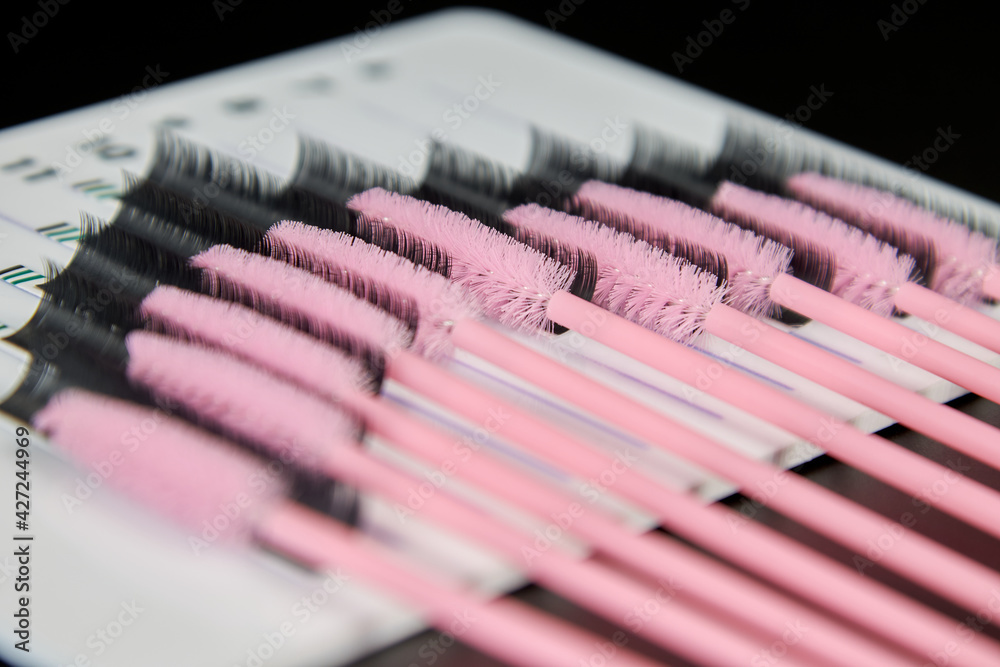 A tablet with false eyelashes and brushes on a black background. Cosmetic accessories for eyelash extensions
