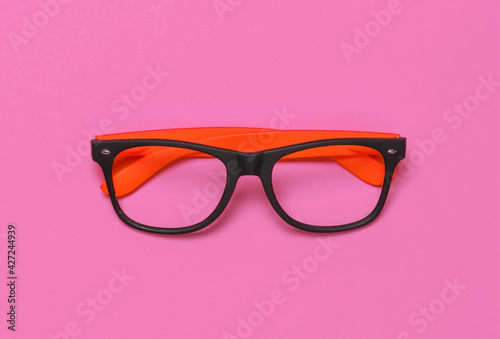 Stylish glasses without lenses on pink background. Top view