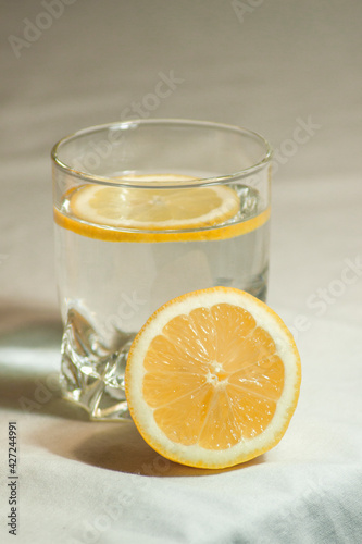 Glass of water with a lemon slice. Lemon cut in half in studio on isolated white background.
