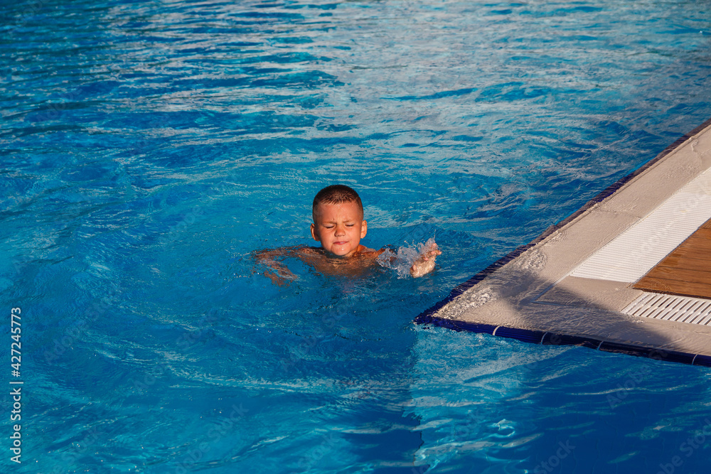 Seven-year-old tanned boy swims in pool squinting