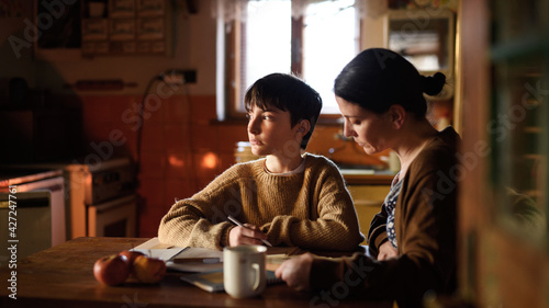 Poor mature mother and small daughter learning indoors at home, poverty concept.