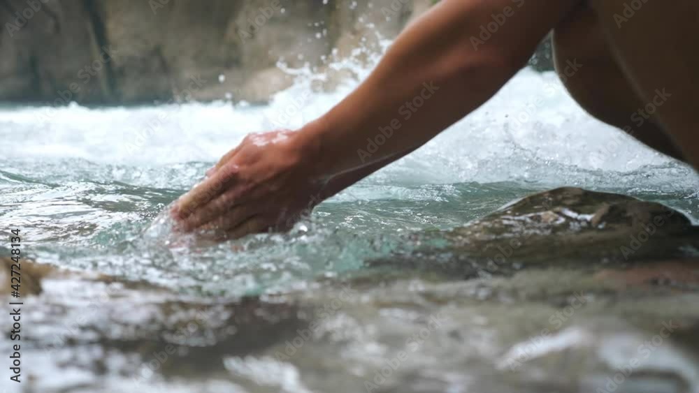 Unrecognizable hiker washing hands in mountain river with clear cool water. Guy standing among river with fast stream and refreshing. Male tourist during his travelling. Blurred background. Slow mo Unrecognizable hiker washing hands in mountain river with clear cool water. Guy standing among river with fast stream and refreshing. Male tourist during his travelling. Blurred background. Slow mo