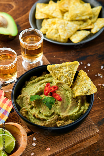 Guacamole. Traditional latinamerican Mexican dip sauce in a black bowl with avocado and ingredients and corn nachos. Avocado spread. Top view. Copyspace