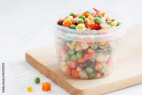 Mix of frozen vegetables in a container on a wooden board.