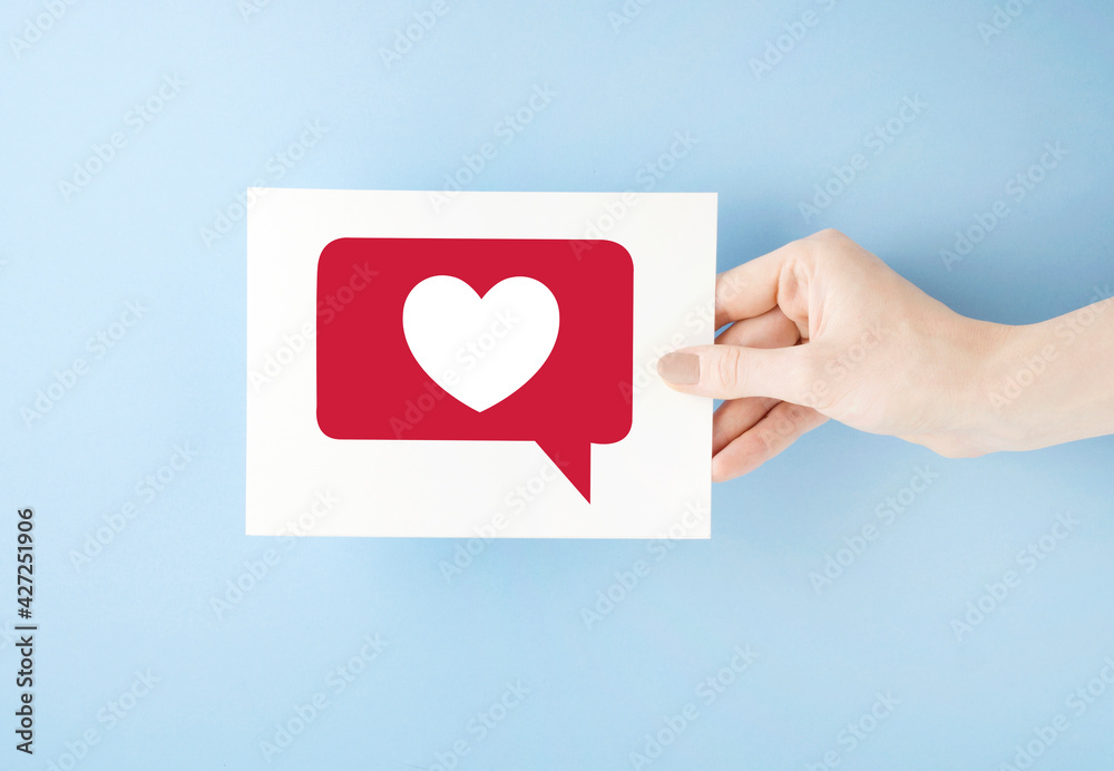 Creative concept photo of hand with list paper with like heart emoji on blue background. Creative concept photo of hand with list paper with like heart emoji on blue background.