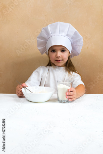A little girl dressed as a cook kneads the dough. Cooking child lifestyle concept. The kid loves, has fun, studies and plays in the kitchen