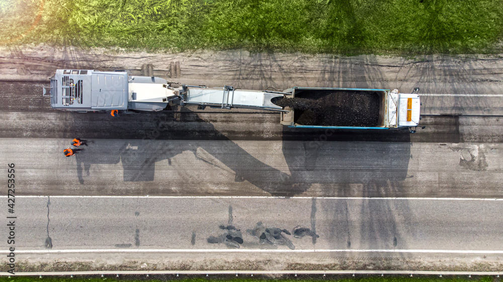 Aerial. Road repair using special equipment. The machine cuts off the top layer of the old asphalt and dumps it into the truck. Top view from drone.