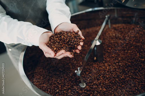 Coffee cooling in roaster machine at coffee roasting process. Young woman worker barista Mixing and hold coffee beans in hands.