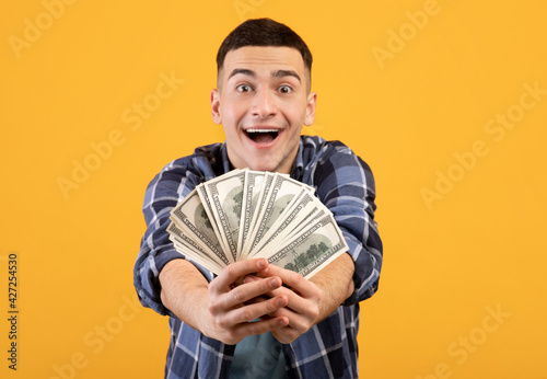 Canvas-taulu Cool hipster guy showing money at camera on orange studio background, selective